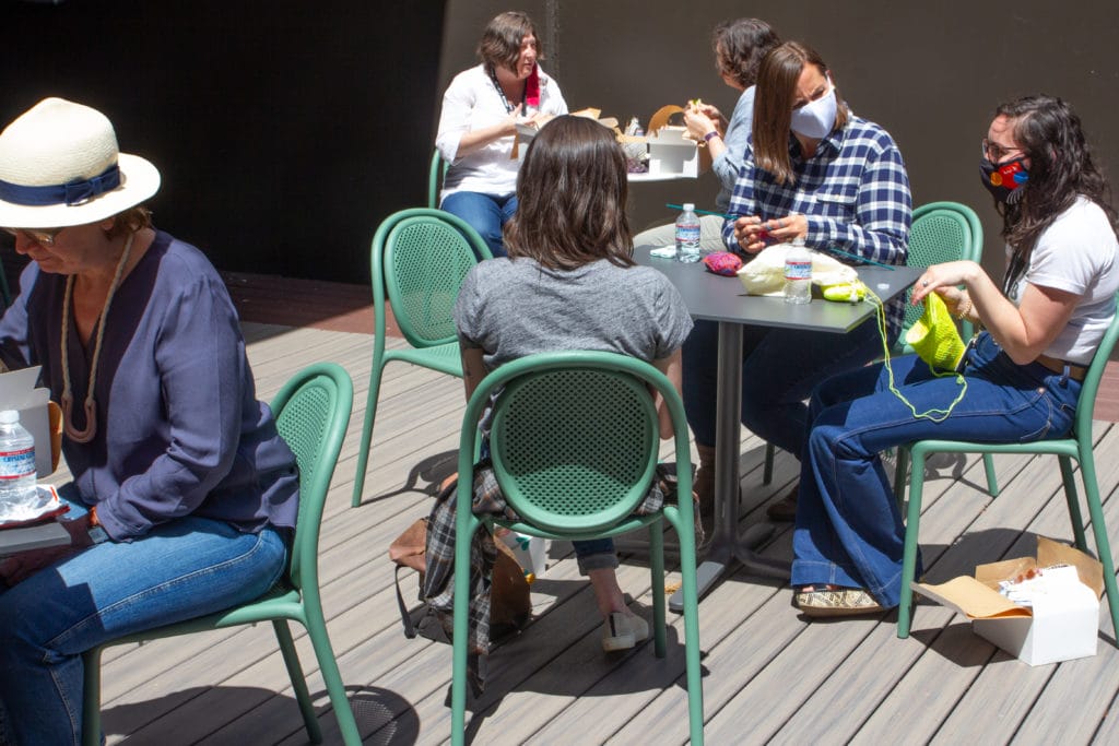 Knitters sitting around a table outdoors and working on knitting projects