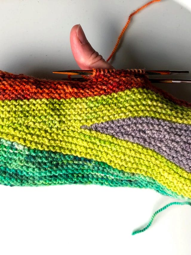 One of Lee's Unfinished Objects: A hand wearing a partially-knitted mitten in green, chartreuse, gray, and red
