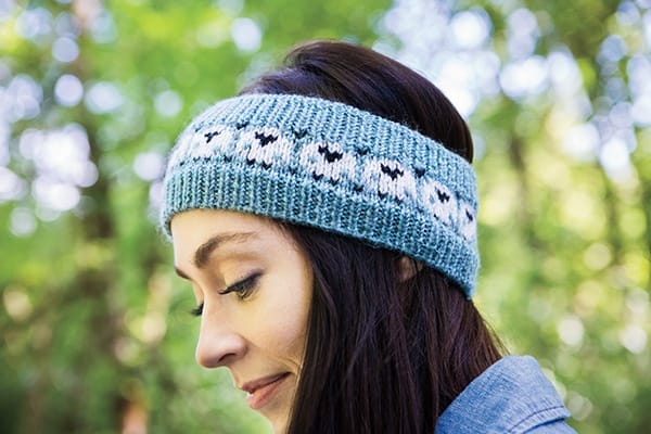 A knitted headband in blue featuring front-views of sheep