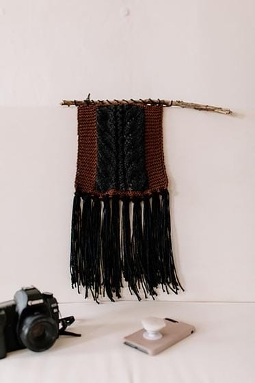 A wall hanging knitted in brown and black, with long fringe