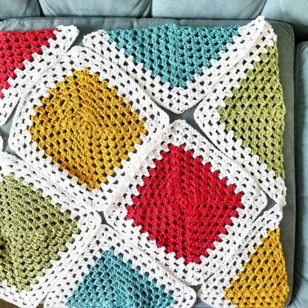 Regular granny squares and triangles are laid out on a couch cushion. They each have a pink, yellow, green, or blue center with a white border.