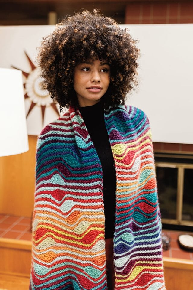 Una toma más cercana de una mujer negra con un afro usando una bata multicolor en una casa de los años 70.