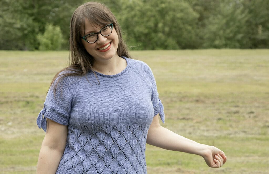 A woman wears a handknit tee with lace details that begin under the bust and short, raglan sleeves with ties at the ends.