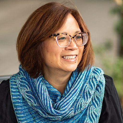 Michele Bernstein, an Asian-American woman, wearing glasses and a brioche shawl
