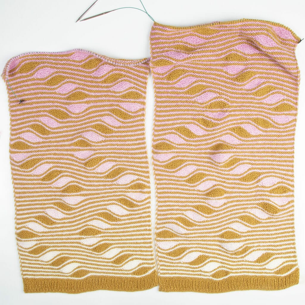 Two halves of a handknit wrap on knitting needles with squiggly stripes in mustard yellow and a cream-to-pink ombre