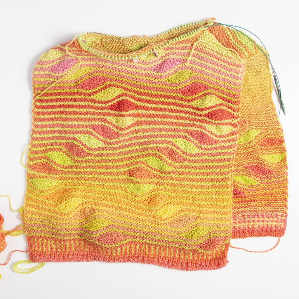 A handknit sweater body with squiggly stripes in yellows, oranges, and pinks