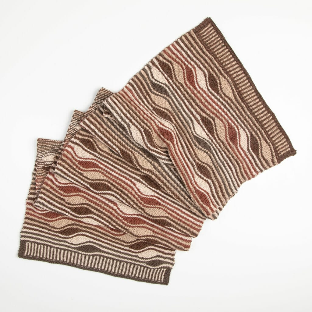 A completed handknit wrap with squiggly stripes in neutral colors