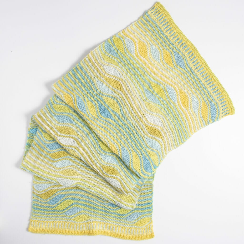 A completed handknit wrap with squiggly stripes in blues, greens, and yellows