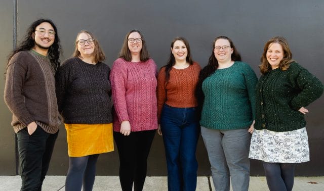 A group of 5 women and one man wearing coordinating cabled sweaters