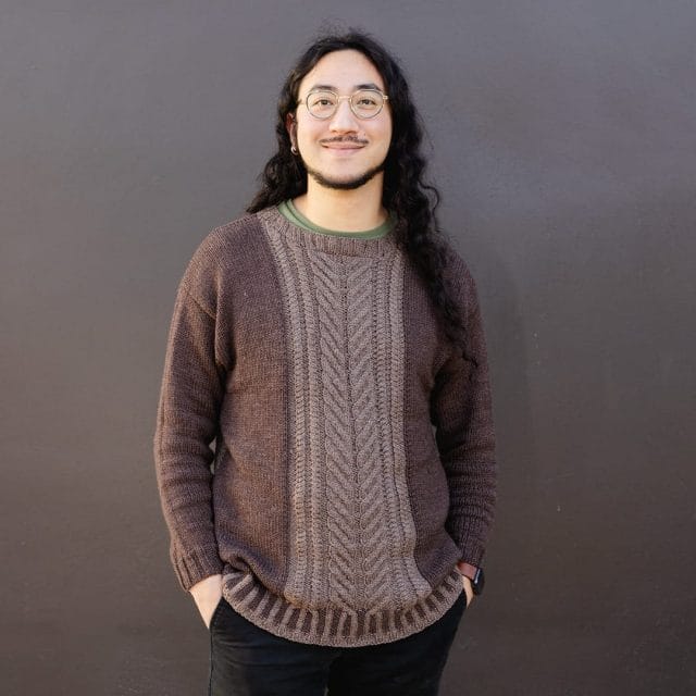 A man wearing a cabled sweater with a contrasting panel